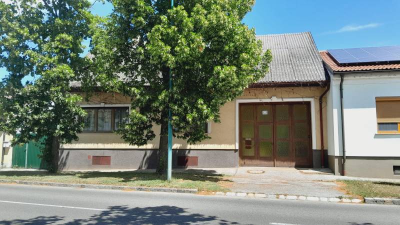 Predaj rodinného domu, Neusiedl am See - Rodinný dom v Potzneusiedli s veľkou bránou a listnatým stromom pred ním.