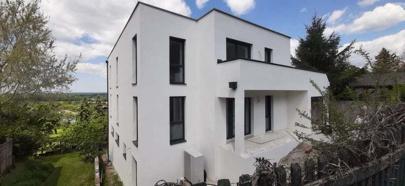 Predaj vily, Bruck an der Leitha - Vila v Hainburgu an der Donau s bielou fasádou, obklopená zeleňou a modrou oblohou.