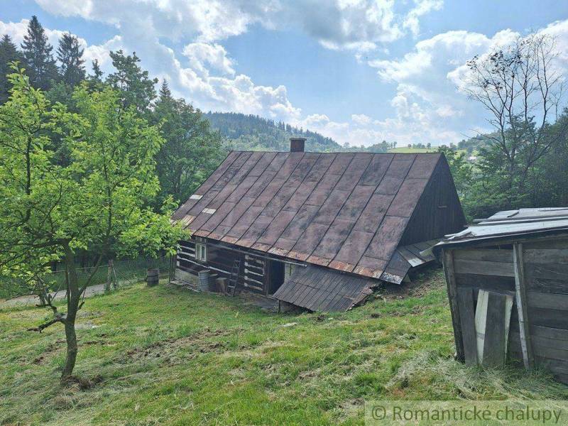 Drevenica v prírodnom prostredí, na okraji obce Zákopčie. - Drevená chata v Zákopčí na svahu, obklopená stromami a modrou oblohou.