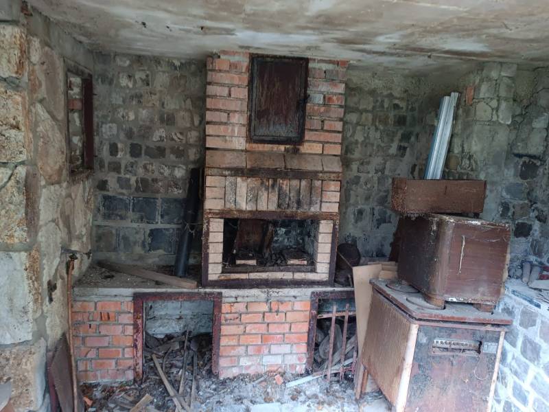 Na predaj rekreačná chata s pozemkom – Nová Baňa (záhradkárska osada) - Opustená miestnosť v chate s tehlovým krbom a skladiskom predmetov.