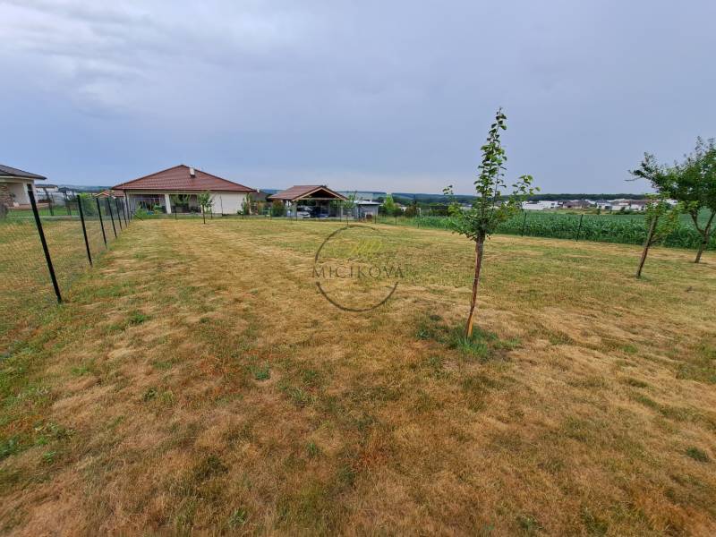 Predáme investičný pozemok, 633 m2, Nitra - Párovské Háje - Pozemok na bývanie v Nitre s trávnikom, plotom a stromami, vzdialené budovy.