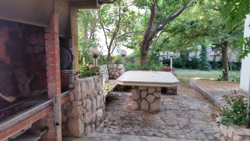CHORVÁTSKO - 2. rad od mora - apartmánový dom - VRSI, Zadar - Dvor rodinného domu vo Vrsi s kamenným stolom a ohniskom obklopený zeleňou.