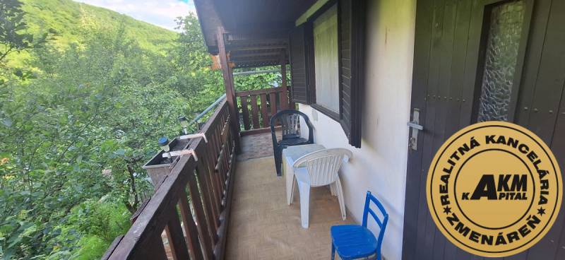Murovaná záhradná chata, 361 m2, Zvolen - Sekier - Drevený balkón chaty vo Zvolene so stolom a stoličkami uprostred zelene.