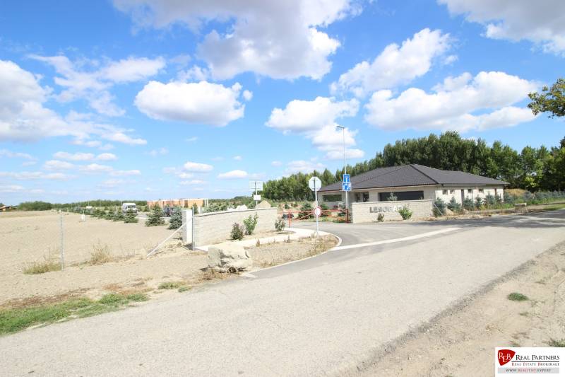 Luxusná veľkometrážna parcela za skvelú cenu Kvetoslavov,2480m2 - Na ulici vidno vstup do oblasti Lesopark, pozemky a bývanie v pozadí.