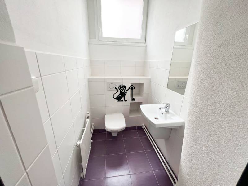 Predaj obchodného priestoru so služobným bytom pri Račianskom Mýte - Toaleta s umývadlom, bielymi obkladačkami a fialovou podlahou na ulici Jozefa Cígera Hronského.
