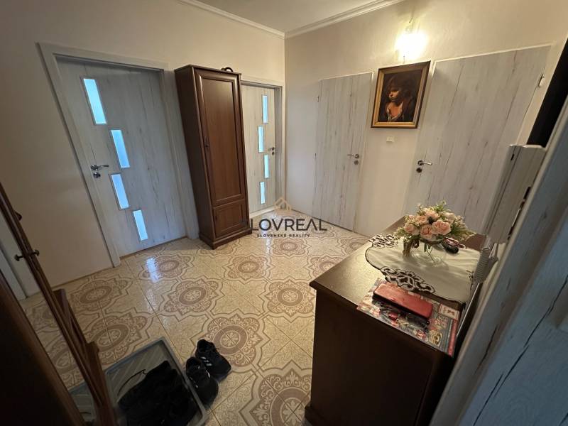 SLOVREAL -PREDAJ 3 IZBOVÝ BYT HANDLOVÁ  - Predsieň v 3-izbovom byte s dekoratívnym kvetinovým aranžmánom a botníkom.