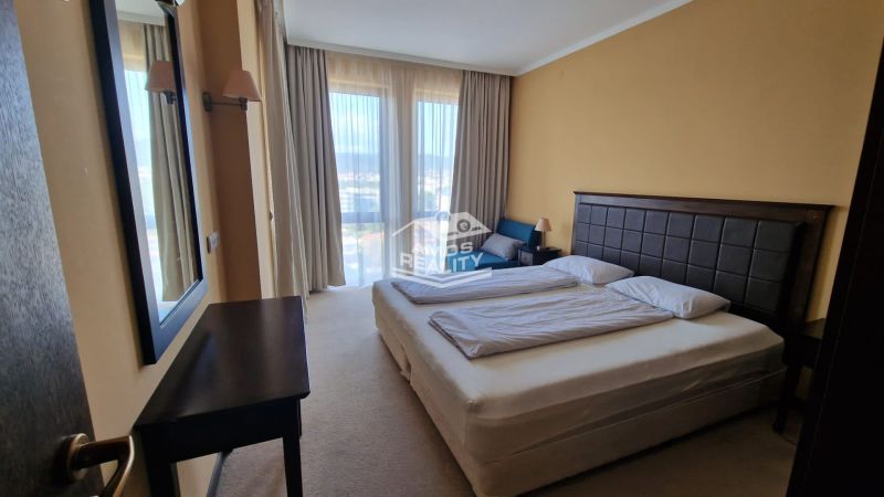 Predaj, 2 i apartmán 72 m2 + balkón výhľad na more, Burgas, BULHARSKO - Spálňa v rekreačnom apartmáne s manželskou posteľou, zrkadlom a výhľadom cez záclony.