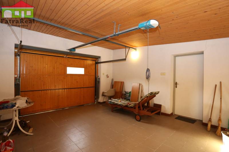 Rodinný dom po kvalitnej rekonštrukcii a prestavbe, Ľubochňa - Garáž v rodinnom dome s drevenou bránou, stropným osvetlením a záhradným ležadlom.