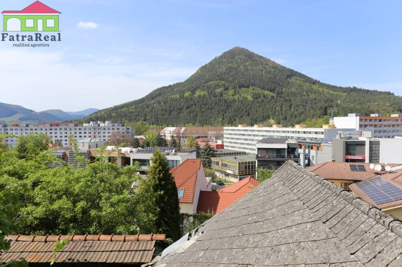 Rodinný dom v rekonštrukcii, Ružomberok - Na ulici Nám. A. Hlinku vidieť strechy, budovy a zalesnený kopec poza Rodinný dom.