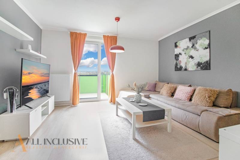 ALL INCLUSIVE REAL I KRÁSNY 2 IZBOVÝ BYT S BALKÓNOM GALANTA WEST - Obývačka 2-izbového bytu so sedačkou, televízorom a balkónom, svetlé závesy a doplnky.