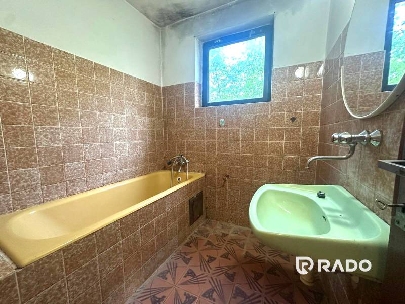 Na predaj Rodinný dom Drietoma – pozemok 745 m2  - Kúpeľňa v rodinnom dome s vaňou a umývadlom, obložená hnedými obkladačkami.
