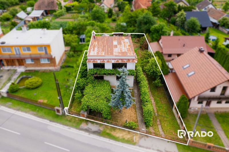 Na predaj Rodinný dom Drietoma – pozemok 745 m2  - Rodinný dom v Drietome obkolesený zeleňou a ďalšími domami, s plechovou strechou.