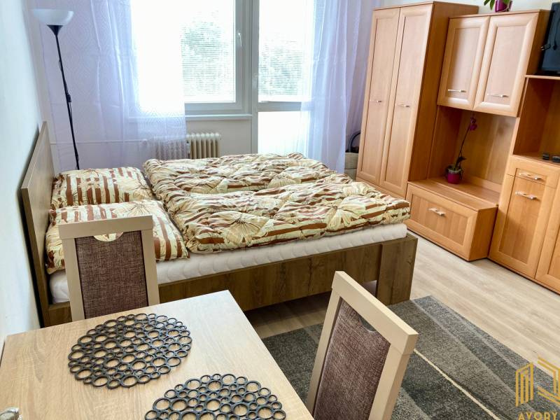 NA PRENÁJOM GARSÓNKA s BALKÓNOM, SENICA, ŠTEFÁNIKOVA UL. - Garsónka s posteľou, stolom a skrinkou s dekoráciou, príjemné zariadenie interiéru.