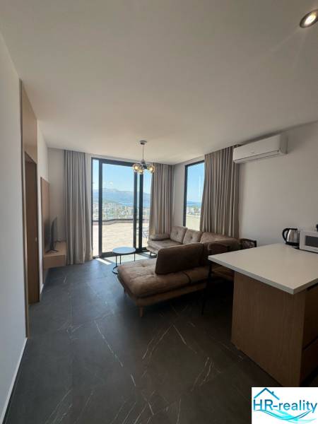 Ksamil – luxusné zariadené apartmány v Maledivách Európy - Obývacia izba v rekreačnom apartmáne s veľkými oknami, pohovkou a kuchynským kútom.