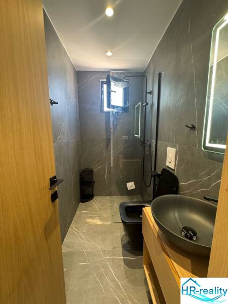 Ksamil – luxusné zariadené apartmány v Maledivách Európy - Kúpeľňa v rekreačnom apartmáne so sprchou, moderným umývadlom a tmavým WC pre pohodlie.