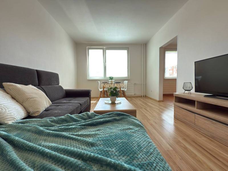 - EXKLUZÍVNE - PREDAJ - 3,5 IZBOVÝ BYT - LEVICE - Svetlá obývačka v 4-izbovom byte s pohovkou, dekou a televízorom.