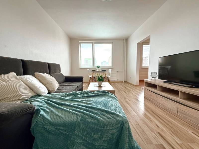 - EXKLUZÍVNE - PREDAJ - 3,5 IZBOVÝ BYT - LEVICE - Obývačka v 4-izbovom byte s pohovkou, stolíkom a televízorom na drevenej podlahe.