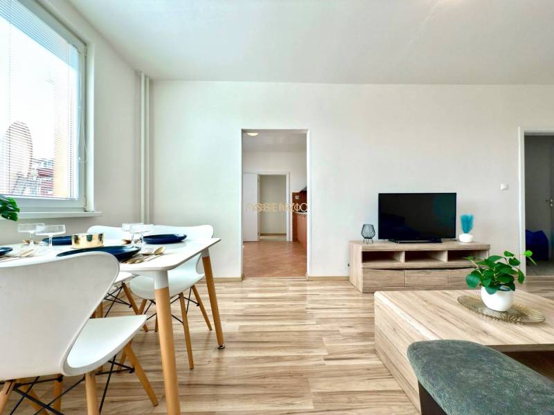 - EXKLUZÍVNE - PREDAJ - 3,5 IZBOVÝ BYT - LEVICE - Obývacia izba v 4-izbovom byte s jedálnym stolom, televízorom a drevenou podlahou.