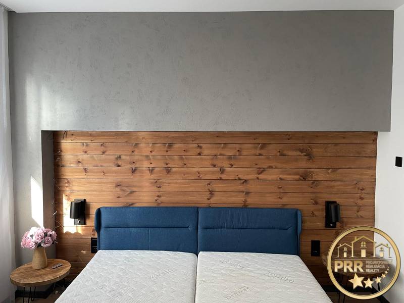 Na predaj krásny komplet prerobený, moderne zariadený 3-izb. byt v BnB - Svetlá spálňa v 3-izbovom byte s drevenou čelnou stenou a modrou posteľou.