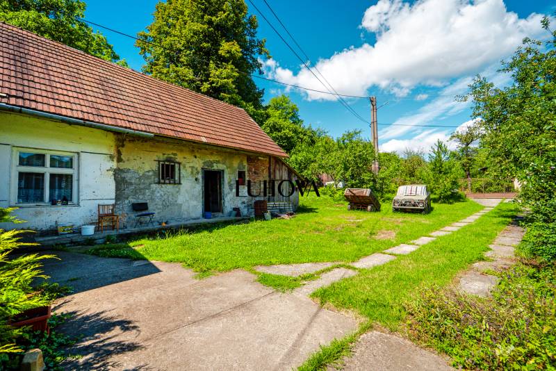 Rodinný dom na rekonštrukciu_Lúky - Rodinný dom na Lúky v Lúky s trávnatým dvorom a stromami v pozadí.