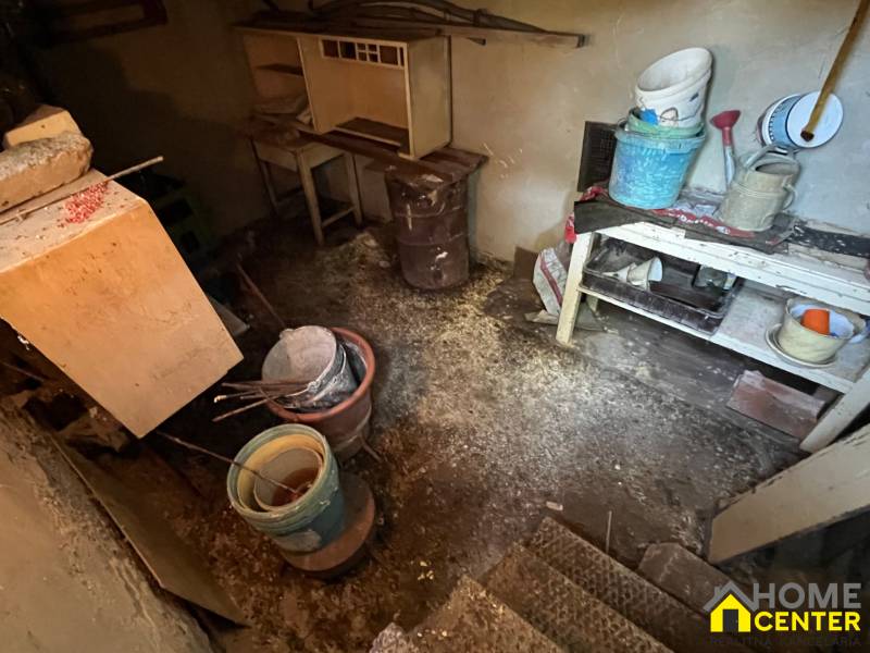NA PREDAJ 4 izb. rodinný dom s veľkým potenciálom v Kolárove - Starý suterén rodinného domu so stolom, vedrami a náčiním v tmavej miestnosti.