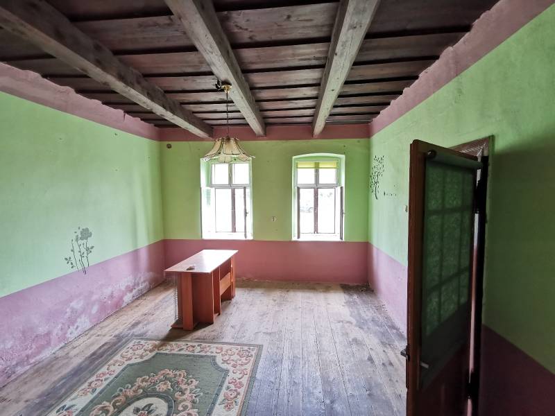 PREDAJ-vidiecky dom s veľkým pozemkom pod lesom, Nitr.Sučany, okr.PD - Izba v rodinnom dome s dreveným stropom, starým stolom a kobercom.