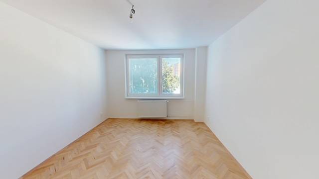 PRENÁJOM - Priestranný moderný 2 izbový byt s 2 balkónmi - Izba s parketami vo svetlom 2-izbovom byte, okno s výhľadom na stromy.