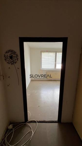✅ SLOVREAL ponúka na predaj Garsónku v obľúbenej lokalite Levice – Ryb - Nezariadená garsónka s oknom, radiátorom a káblami na zemi.
