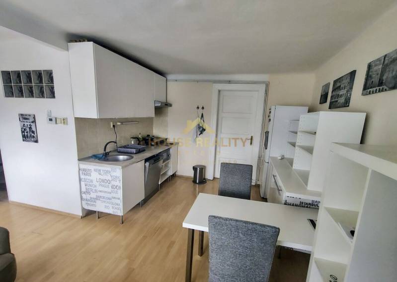 Prenájom pekný 2 izbový, Špitálska ulica, Bratislava I. Staré Mesto - Kuchyňa v 2-izbovom byte s jedálenským stolom, bielymi skrinkami a drevenou podlahou.
