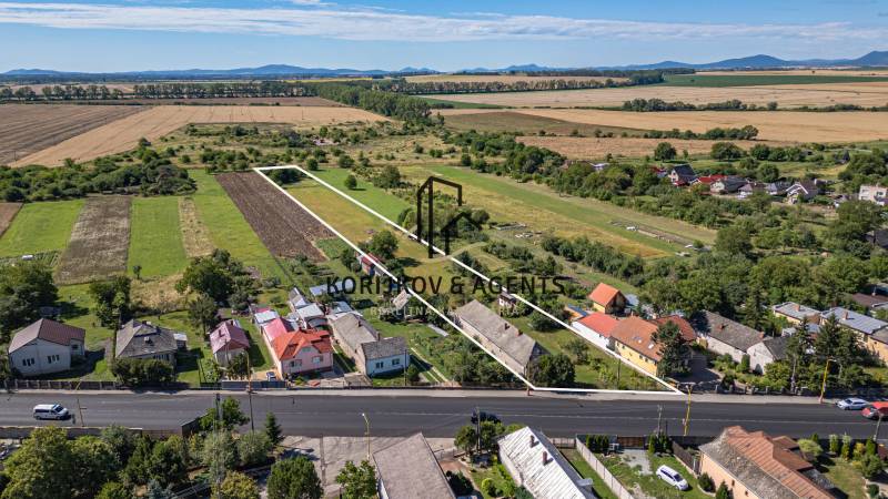 PREDAJ, Pozemok s rodinným domom Sečovce, okres Trebišov - Pozemky na bývanie v Sečovciach, zelené polia, niekoľko domov a veľká cesta vpredu.