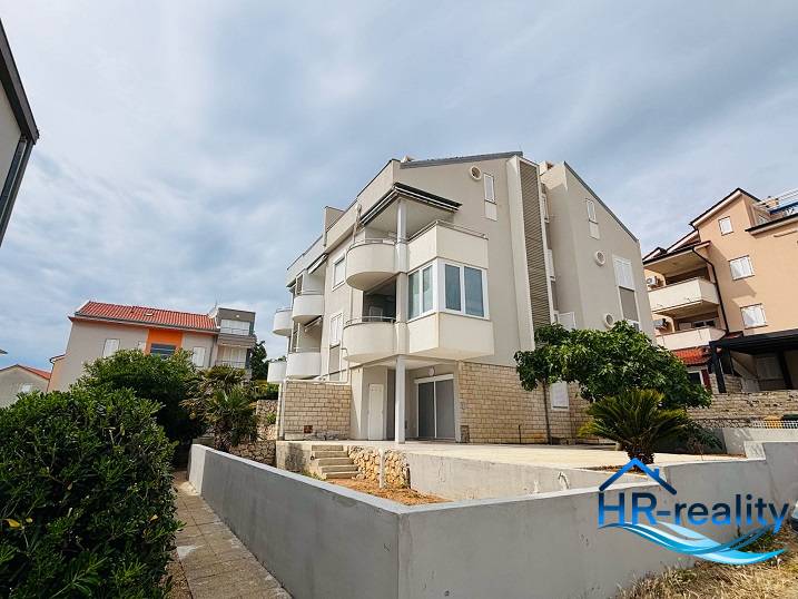 ☀NOVALJA (HR) - 3-izbový moderne zariadený apartmán, blízko pláže  - Bytový dom s balkónmi v Novalji, 3-izbové byty, obklopený zeleňou a kríkmi.