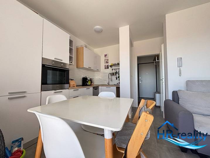 ☀NOVALJA (HR) - apartmán s pekným výhľadom na more  - Kuchyňa v 2-izbovom byte s bielymi spotrebičmi a dreveným jedálenským stolom.