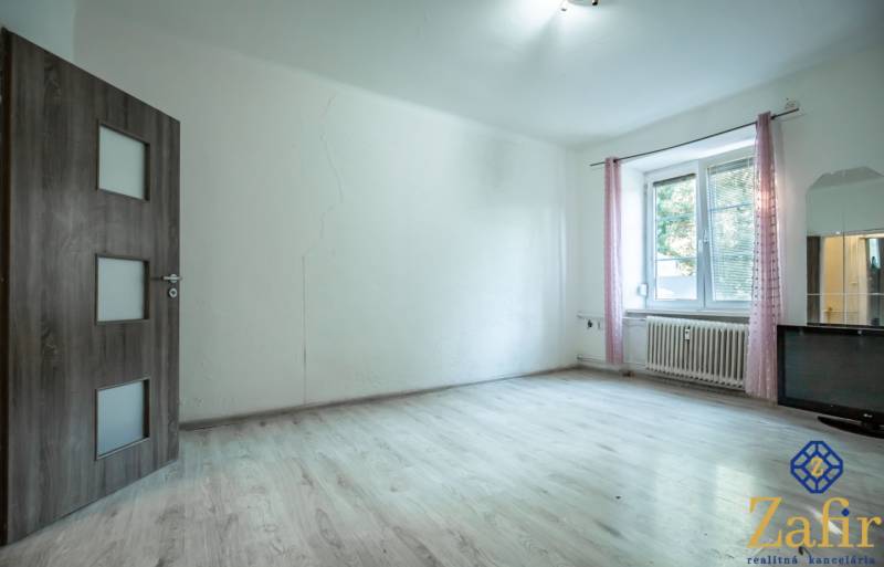 3 IZBOVÝ BYT 89,14 m2 VHODNÝ NA REKONŠTRUKCIU, ALE OBÝVATEĽNÝ UŽ TERAZ - Svetlá miestnosť s drevenou podlahou a oknom v 3-izbovom byte.