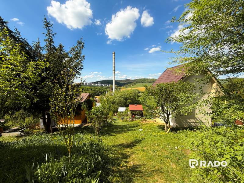 Na predaj záhrada, Trenčín-Chrasť - Záhrady v Trenčíne s výhľadom na komín, oblohu a zeleňou všade navôkol.