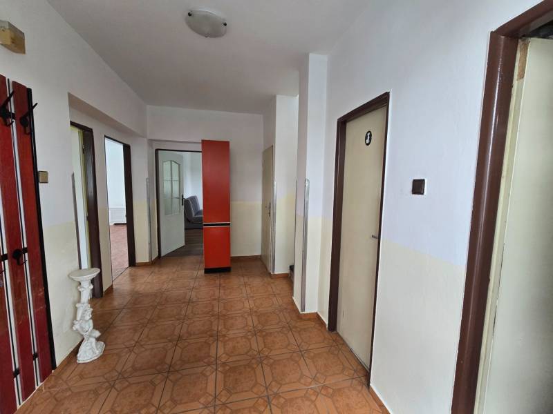 Veľký 6 izbový rodinný dom - Rakoľuby - Chodba v rodinnom dome s hnedou podlahou, červená skriňa, biele steny.