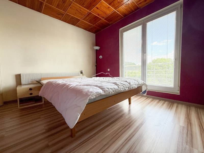 Na prenájom, 5-izbový rodinný dom s pozemkom 2225 m2, Papradno - Svetlá spálňa v rodinnom dome s dreveným stropom a veľkým oknom.