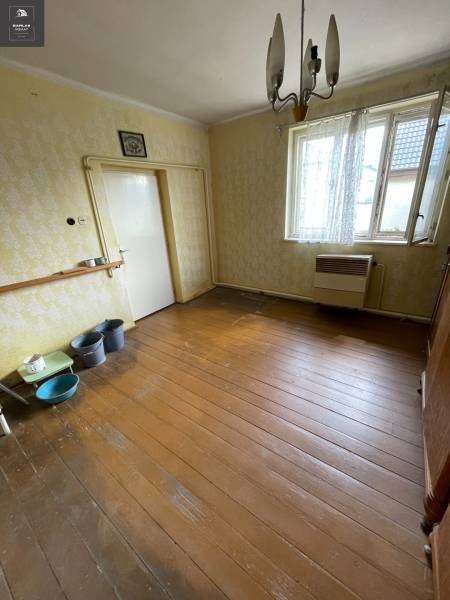 Ponúkame na predaj starší rodinný domček v Trenčianskych Stankovciach - Interiér rodinného domu s drevenou podlahou, starším nábytkom a zaveseným svietidlom.