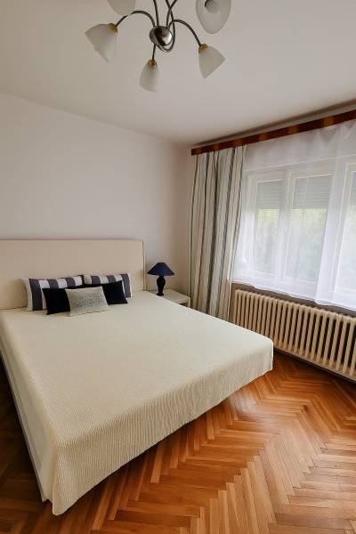 5 izbový rodinný dom Topoľčianky - Svetlá spálňa v rodinnom dome s posteľou, lampou a drevenou podlahou.