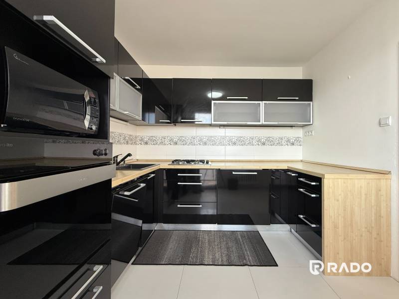 Priestranný 3-izbový byt s balkónom 68 m² Belinského - Kuchyňa v 3-izbovom byte s čiernymi skrinkami a drevenou pracovnou doskou.