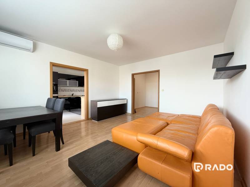 Priestranný 3-izbový byt s balkónom 68 m² Belinského - Obývacia izba v 3-izbovom byte s oranžovou sedačkou a jedálenským stolom.
