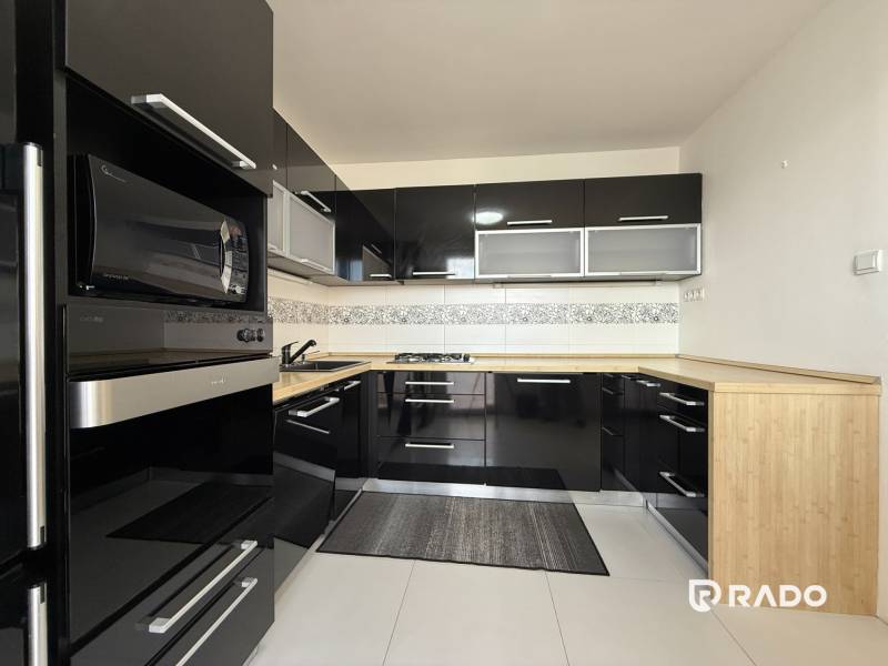 Priestranný 3-izbový byt s balkónom 68 m² Belinského - Čierna kuchyňa so zabudovanými spotrebičmi a drevenou pracovnou doskou v 3-izbovom byte.