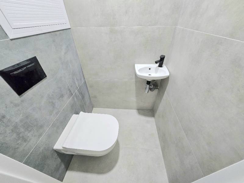 3 izbový byt Bánovce nad Bebravou / CENTRUM- STRED / 56 m2 / NOVÁ REKO - Kúpeľňa v 3-izbovom byte s toaletou a umývadlom, obložená šedými dlaždicami.