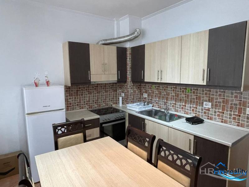 Sarandë - novozariadený apartmán v tesnej blízkosti mora - Kuchyňa v Rekreačnom apartmáne s jedálenským stolom a bielymi spotrebičmi.