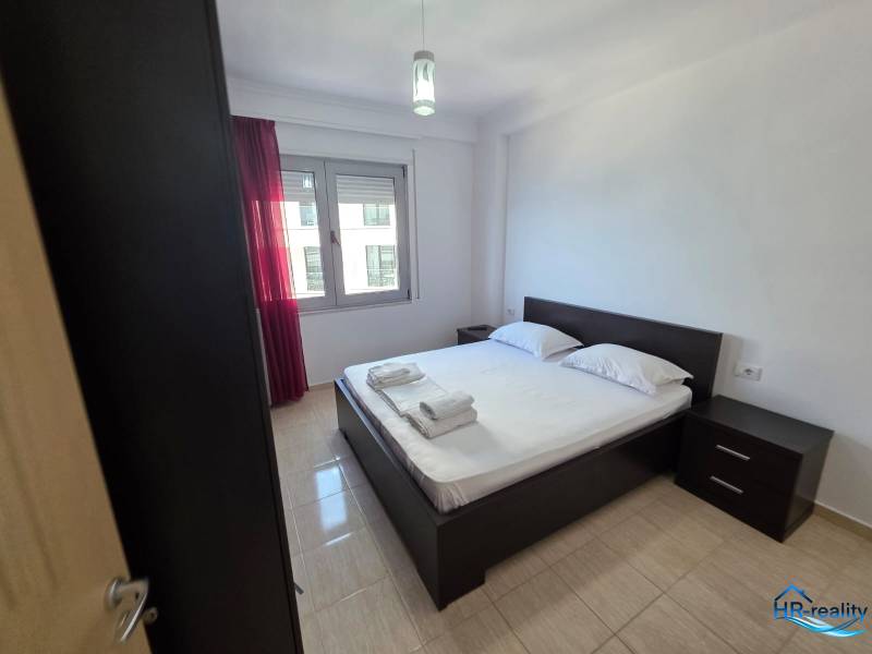 Sarandë - zariadený apartmán s otvoreným výhľadom na more - Spálňa v rekreačnom apartmáne s dvojlôžkom, nočnými stolíkmi a oknom s červenými závesmi.