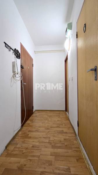 Predaj 3i byt, nepriechodné izby, Osuského ul., BA - Petržalka - Háje - Chodba s drevenou podlahou v 3-izbovom byte, s dverami a závesným háčikom.