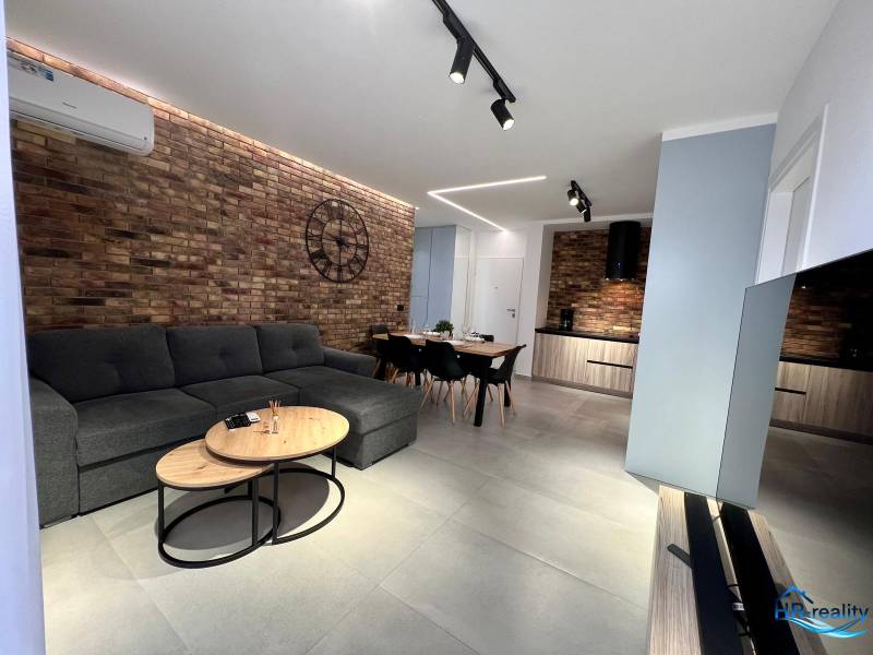 Sarandë - zariadený apartmán, výhľad na more, garážové státie - Obývacia izba v rekreačnom apartmáne s tehlovou stenou, sedačkou a televízorom.