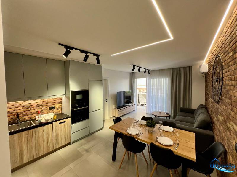 Sarandë - zariadený apartmán, výhľad na more, garážové státie - Obývačka s kuchyňou v Rekreačnom apartmáne. Tehlová stena, jedálenský stôl a pohodlná sedačka.