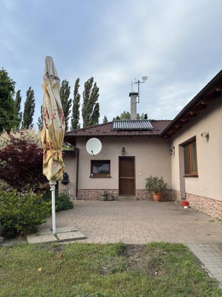 Priestranný rodinný dom v Malackách + pozemok na výstavbu RD v cene - Rodinný dom v Malackách, predný dvor s terasou, zeleňou a satelitnou anténou.