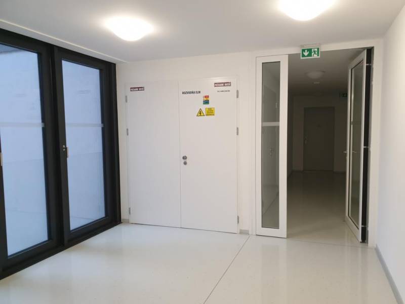 Nový moderný byt s balkónom a parkovaním v širšom centre. Jarabinková - Biela chodba s dverami, oknami a označením bezpečnostných pokynov v 2-izbovom byte.