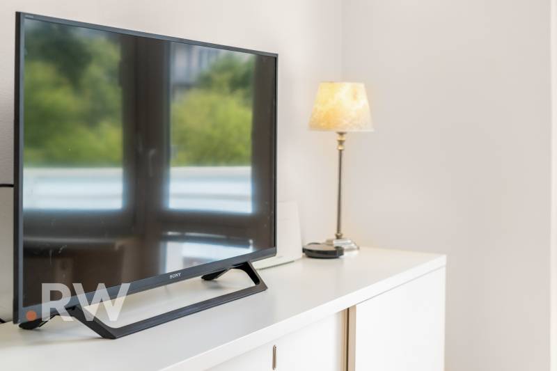 REWIN I VÝNIMOČNÝ 2-IZBOVÝ BYT NA PRENÁJOM! - Televízor a lampa na bielej komode v 2-izbovom byte.